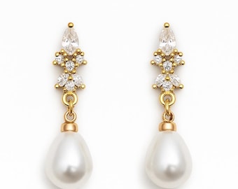 May include: A pair of gold-toned drop earrings. Each earring features a pear-shaped white pearl suspended below a cluster of clear, sparkling crystals and a teardrop-shaped crystal at the top. The earrings are set against a white background.