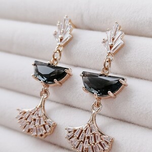 Può includere: Un paio di orecchini pendenti color oro. Ogni orecchino presenta una pietra a forma di mezzaluna grigio scuro, un gruppo di cristalli rettangolari trasparenti e un design a forma di ventaglio con cristalli trasparenti più piccoli.