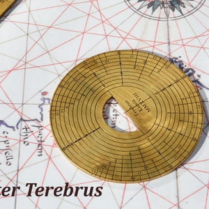 Peut inclure: Un outil circulaire en laiton avec un trou au centre et des marques autour du bord. L'outil est étiqueté "MMXVIII Kidvia Terforus".