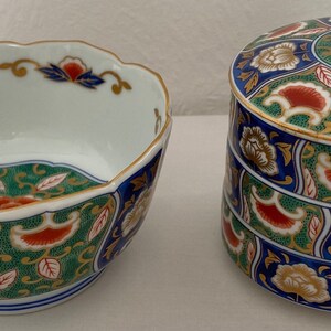 May include: A decorative ceramic bowl and a lidded container. The bowl has a scalloped rim and the container is cylindrical. Both are white with blue, green, red, and gold floral patterns. The bowl is approximately 15 cm in diameter.