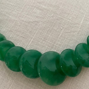 May include: A green necklace with large, polished, round beads. The beads vary in size, creating a graduated design. The necklace is made of a glossy, jade-like material, and the beads are strung together.