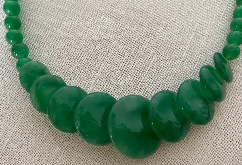 May include: A green necklace with large, polished, round beads. The beads vary in size, creating a graduated design. The necklace is made of a glossy, jade-like material, and the beads are strung together.