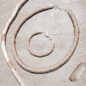 Op de afbeelding: Een set van twee bruine touwkettingen met zilveren sluitingen. De grotere ketting is langer dan de kleinere.