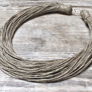 Puede incluir: Un collar largo y grueso hecho de cordón de lino beige natural. El cordón está retorcido y anudado en los extremos para crear un diseño simple y elegante.