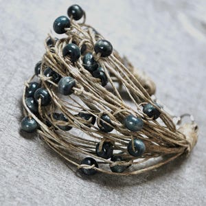 May include: A bracelet made of natural twine with dark blue wooden beads. The bracelet is woven with multiple strands of twine and has a simple clasp.