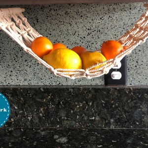 May include: A white macrame hammock hanging from a kitchen cabinet, filled with lemons and oranges. The hammock is labeled "Patchwork".