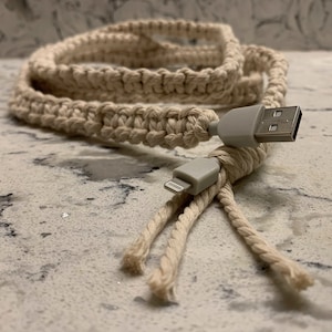 Pode incluir: Um cabo trançado branco envolto em torno de um cabo de carregamento branco com um conector USB-A em uma extremidade e um conector Lightning na outra extremidade.