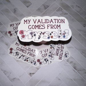 May include: A white sticker with the text "My validation comes from myself" in red and black lettering. The text is surrounded by a border of pink, blue, and yellow flowers.