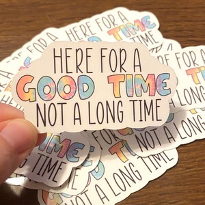 May include: A stack of white stickers with a rainbow tie-dye design. The stickers feature the text "Here for a good time, not a long time".