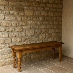 May include: A wooden bench with a natural finish. The bench has a rectangular seat and four turned legs. The bench is set against a stone wall and a tiled floor. The wood has a warm, medium brown tone.