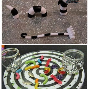 Könnte beinhalten: Miniaturfiguren eines Sandwurms, eines segmentierten Wurms und eines Kopfes mit einem schwarz-weißen Streifendesign. Das untere Bild zeigt einen weißen Teller mit einem schwarz-grünen Spiraldesign, umgeben von bunten Gummibonbons und zwei kleinen Gläsern.