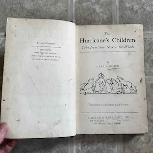 May include: Open book with aged pages. The title page reads "The Hurricane's Children" by Carl Carmer. An illustration depicts a person with wolves. The book is published by Farrar & Rinehart, Inc.