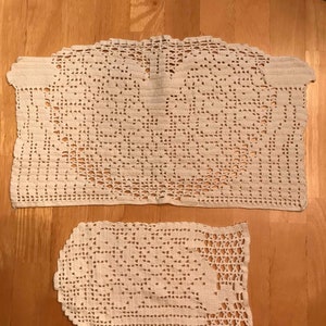 Puede incluir: Dos manteles individuales de ganchillo de color crema. El mantel individual más grande es rectangular y el más pequeño es un rectángulo con esquinas redondeadas.