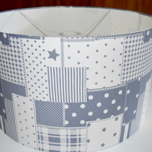 Może przedstawiać: Biały klosz lampy z patchworkowym wzorem w odcieniach szarości i bieli. Wzór zawiera gwiazdy, kropki, paski i kratę.