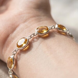 Pode incluir: Uma pulseira de corrente de prata com várias pedras preciosas de citrino amarelo de formato oval e facetadas. Cada pedra é engastada numa moldura de prata lisa e ligada por pequenos elos circulares de prata.