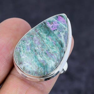 Peut inclure: Bague en argent ornée d'une grosse pierre en forme de goutte d'eau. La pierre présente un aspect marbré avec des nuances de vert, de violet et de blanc. L'anneau est en argent poli.