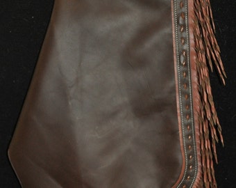 May include: Brown leather chaps with fringe and a tooled design. The chaps have a belt loop and a silver concho.