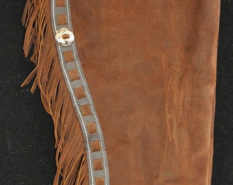 May include: Brown leather chaps with fringe detail and a decorative top flap. The chaps have a black leather trim with white stitching and silver conchos.