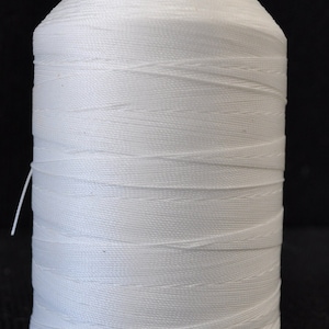 May include: A spool of white thread wound around a black plastic bobbin.