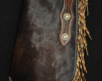 May include: Brown leather chaps with a fringe bottom and silver conchos. The chaps are made of a soft, supple leather and have a classic western style.