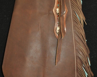 May include: Brown leather chaps with turquoise fringe and a decorative stitching design. The chaps have a belt loop and a buckle.