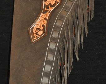 May include: Brown leather chaps with fringe and intricate leaf designs. The chaps have a white stitching detail and a belt loop.
