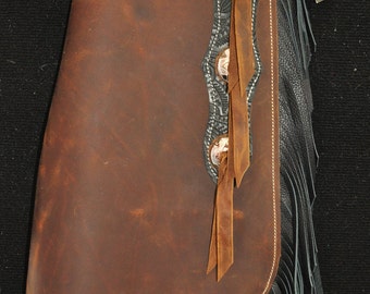 May include: Brown leather chaps with black fringe and decorative stitching. The chaps have three silver conchos with brown leather straps.