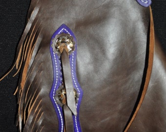 Può includere: Chaps in pelle marrone con cuciture viola e bianche, frange e dettagli metallici decorativi.