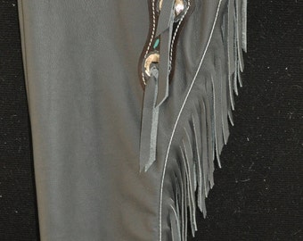 May include: Gray leather chaps with fringe and turquoise stitching. The chaps have a decorative design with silver accents and a belt loop.