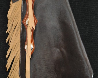 May include: A pair of brown leather chaps with a tan fringe and silver conchos. The chaps have a belt loop and a buckle.