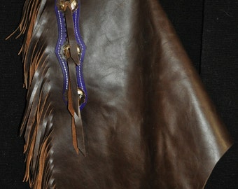 May include: Brown leather chaps with fringe and purple stitching. The chaps have a decorative top with a woven design and a belt loop.