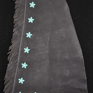 May include: Black leather chaps with a turquoise suede top and fringe. The chaps are decorated with turquoise flower accents.
