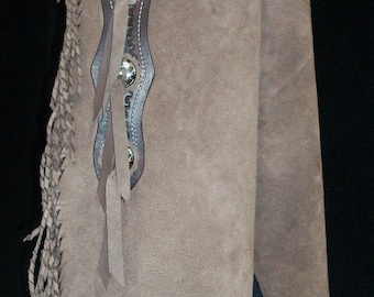 May include: Brown leather chaps with fringe detail and silver conchos. The chaps have a suede-like texture and are worn over jeans.