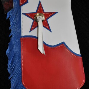 May include: Red and white leather chaps with blue fringe. The chaps have a star design and a white strap with a metal buckle.