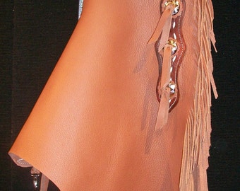 May include: Brown leather chaps with fringe and white stitching. The chaps have a belt loop and a decorative design on the top.