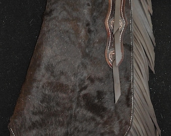 May include: Brown leather chaps with fringe and a tooled design. The chaps have a belt loop and a buckle.