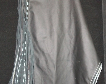 May include: Black leather chaps with white stitching and fringe. The chaps have a zipper on the side and a belt loop at the top.