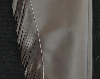May include: Dark brown leather chaps with decorative floral tooling and fringe. The top portion features a light brown border with white stitching and silver accents. A tag is attached to the top.