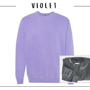 May include: A purple sweatshirt with a crew neck. A second sweatshirt is folded on top of the first sweatshirt. The second sweatshirt is dark gray with white embroidery that says "Mama" and "Jameson, Jonah, Scotlyn".