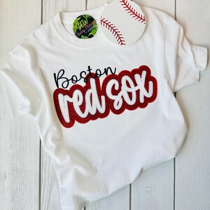 May include: White t-shirt with a red and white embroidered design that says "Boston Red Sox".