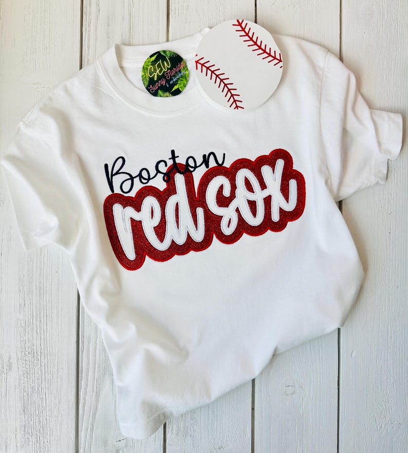 May include: White t-shirt with a red and white embroidered design that says "Boston Red Sox".