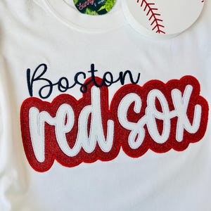 May include: White t-shirt with red and white embroidered text that says "Boston Red Sox".