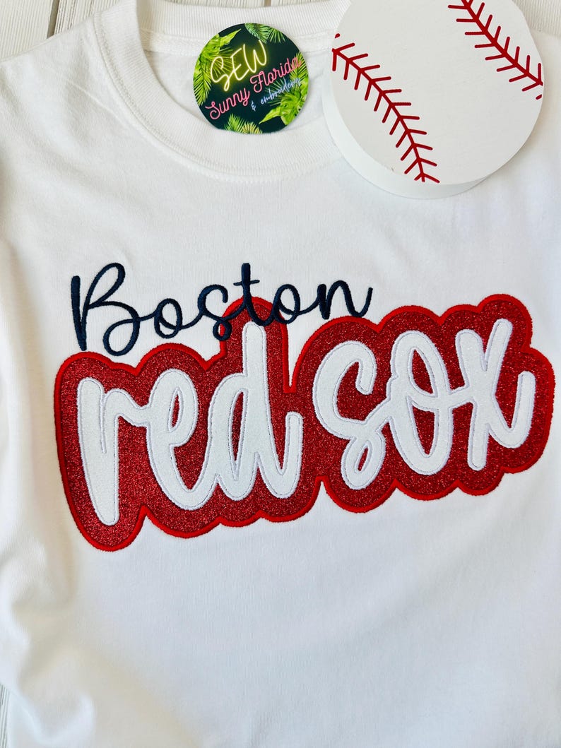 May include: White t-shirt with red and white embroidered text that says "Boston Red Sox".