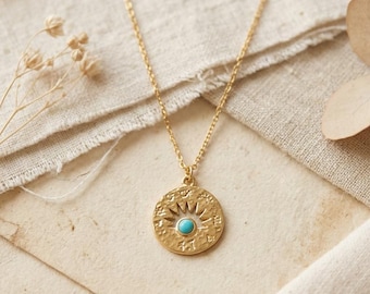 May include: A gold-toned necklace featuring a circular pendant with a sunburst design and a small, round, bright blue stone at its center. The pendant hangs from a delicate gold-toned chain, showcasing intricate engraved details on the metal surface.