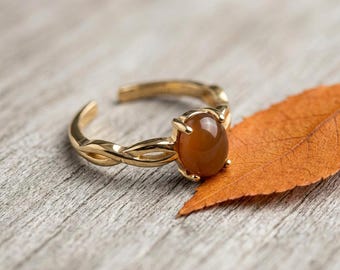 May include: A gold-toned ring featuring a smooth, oval-shaped amber-colored stone set in a prong setting. The band has a twisted, open design that allows for adjustment, showcasing a polished metallic finish and a warm, translucent gemstone.