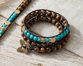 May include: A multi-wrap bracelet featuring brown wooden beads, bright turquoise beads, and small gold-toned metal discs and ribbed beads. The bracelet is secured with a four-petaled flower-shaped metal clasp and black leather cord.