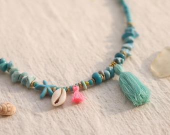 May include: A beaded necklace featuring turquoise-colored stone chips, a small blue starfish charm, a white cowrie shell, a tiny pink tassel, and a larger light blue thread tassel, all strung together with small gold-toned spacer beads.