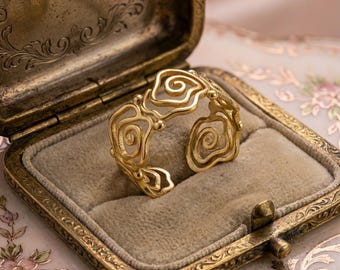 May include: A gold-toned open ring featuring a series of interconnected, swirling, organic wire-like patterns. The band is constructed from thin, polished metal loops that form a continuous, airy, and openwork design around the finger.