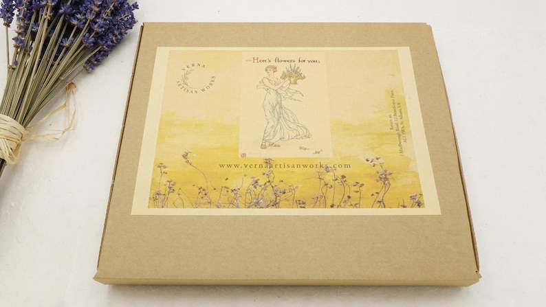 May include: A brown cardboard box with a decorative label featuring an illustration of a woman holding flowers. The label has the text "Here's flowers for you" and the website address "www.verdaartisanworks.com". A bundle of dried lavender is on the left.