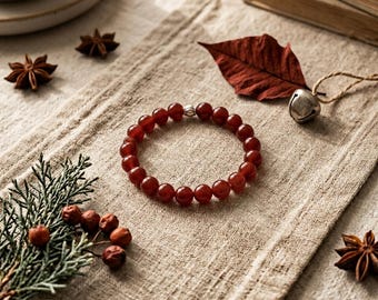 May include: A circular beaded bracelet featuring smooth, polished dark red gemstone beads and a single small silver-toned metal spacer bead. The bracelet is arranged in a round shape, showcasing the uniform size and deep crimson color of the stones.